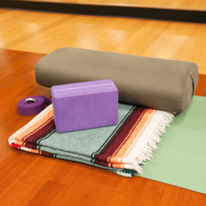 Assisted stretching equipment: grey bolster, purple yoga blocks, a striped blanket, a purple yoga strap laying on top of a green yoga mat